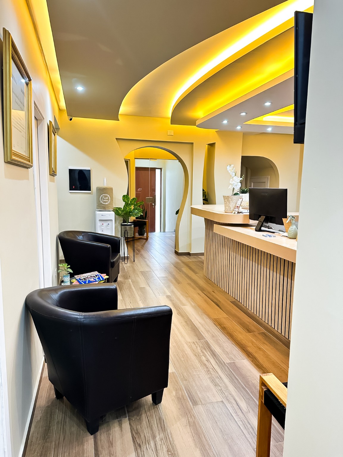Recepción del consultorio, con mostrador de madera, sillones negros y luz cálida.